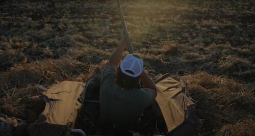 Jon waiting shotgun while sitting in a duck blind in a field