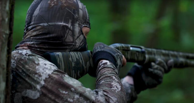 Adam Weis wearing a camo hood while looking down a shotgun