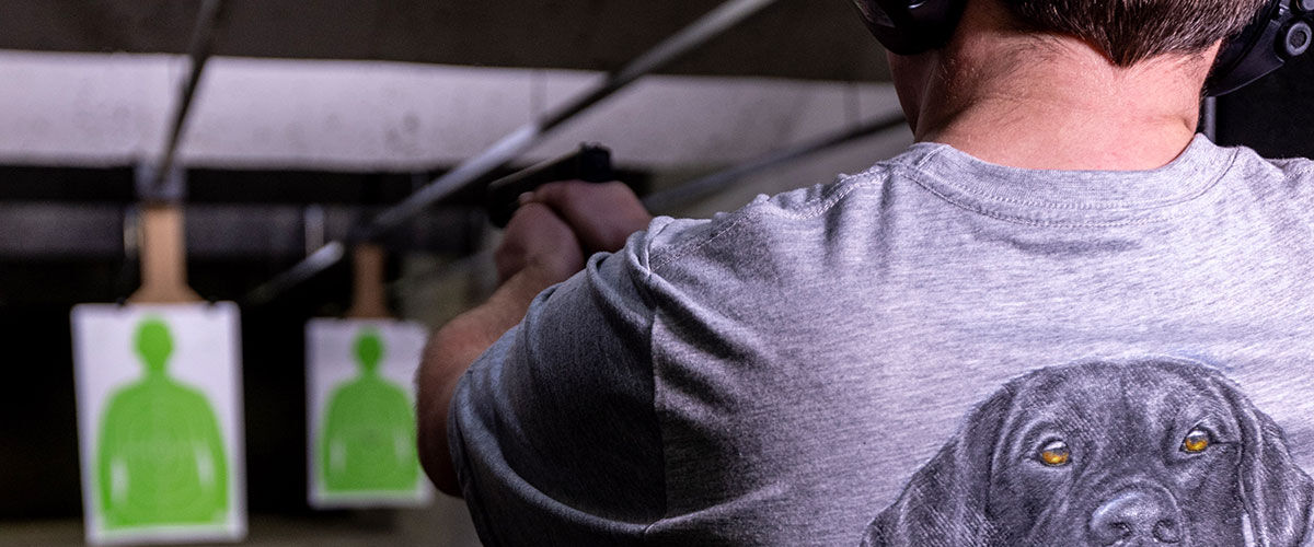 shooter at an indoor range aiming handgun at a paper target