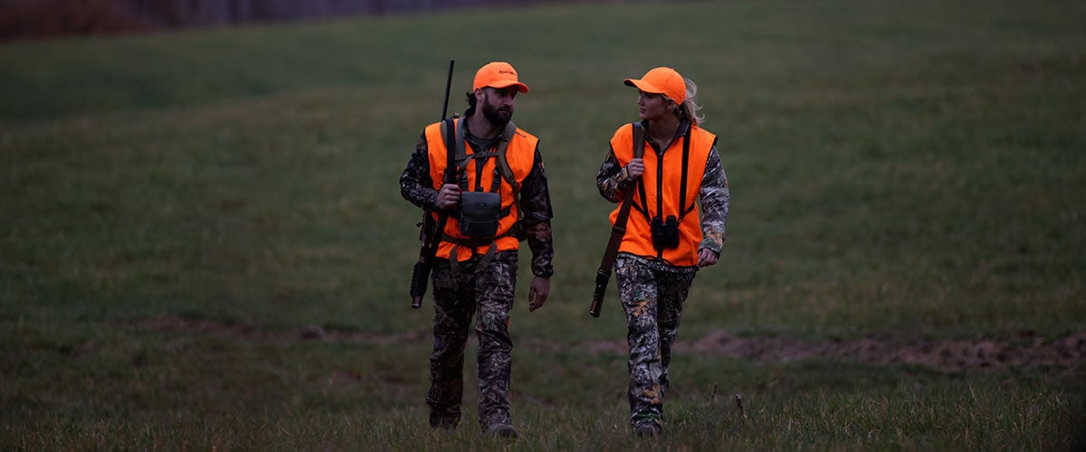 two hunters walking in a field with rifles on their shoulders
